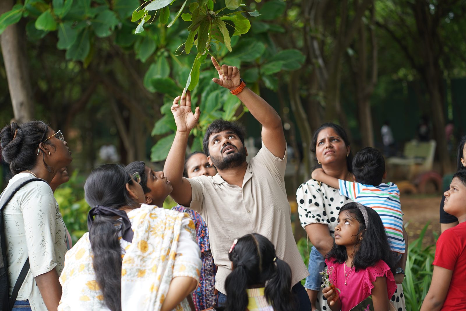 An educator points up at leaves while children and parents look on