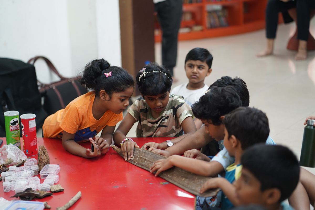 Children run their hands along a giant seed pod at a library session