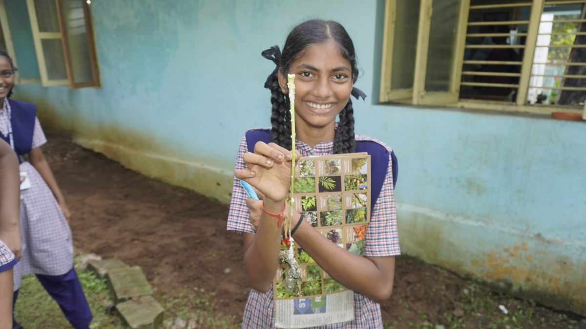 A smiling schoolgirl holds up a stem she found in the school garden