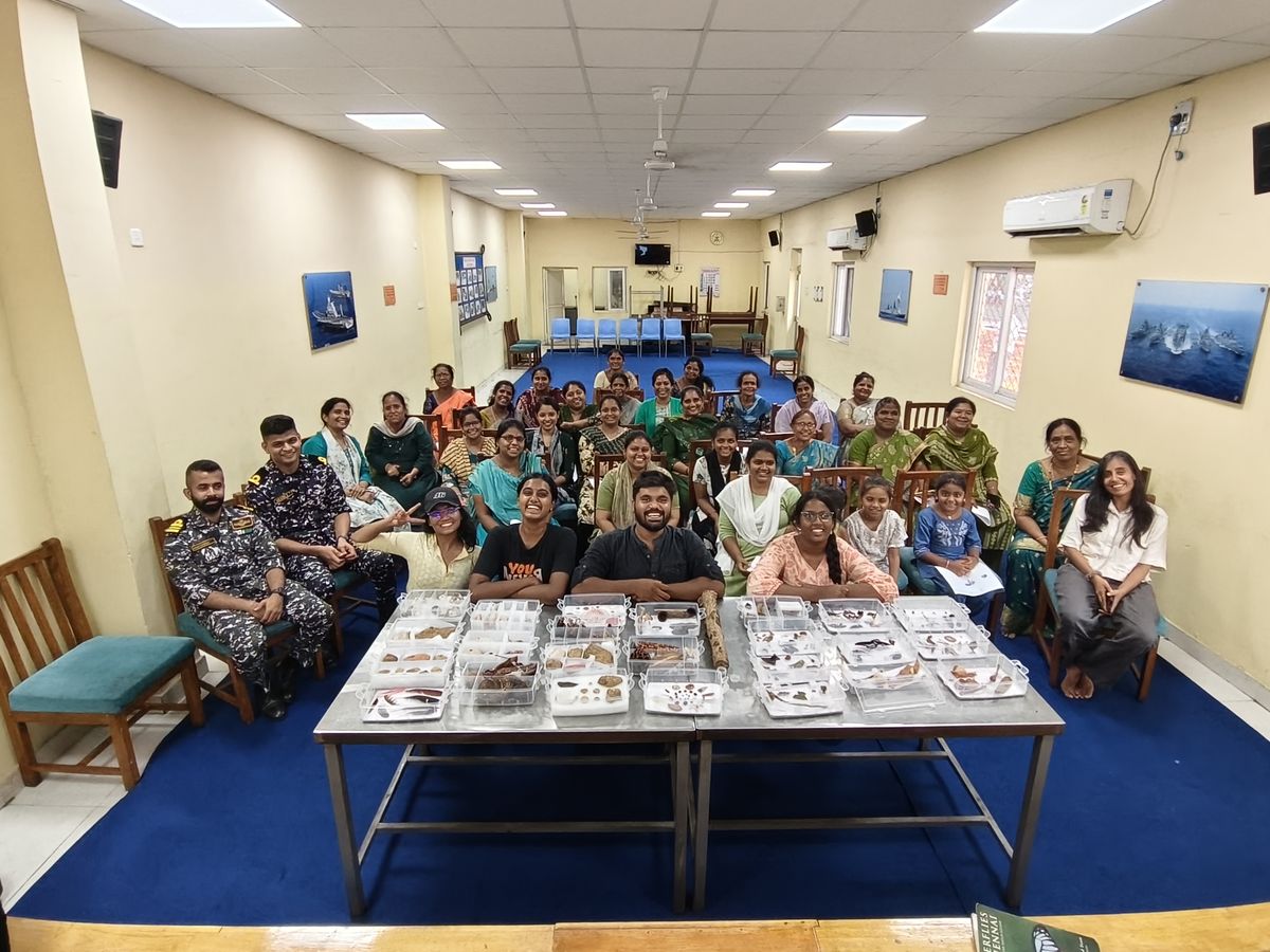 A hall full of smiling participants, including two naval officers, behind tables of specimen trays
